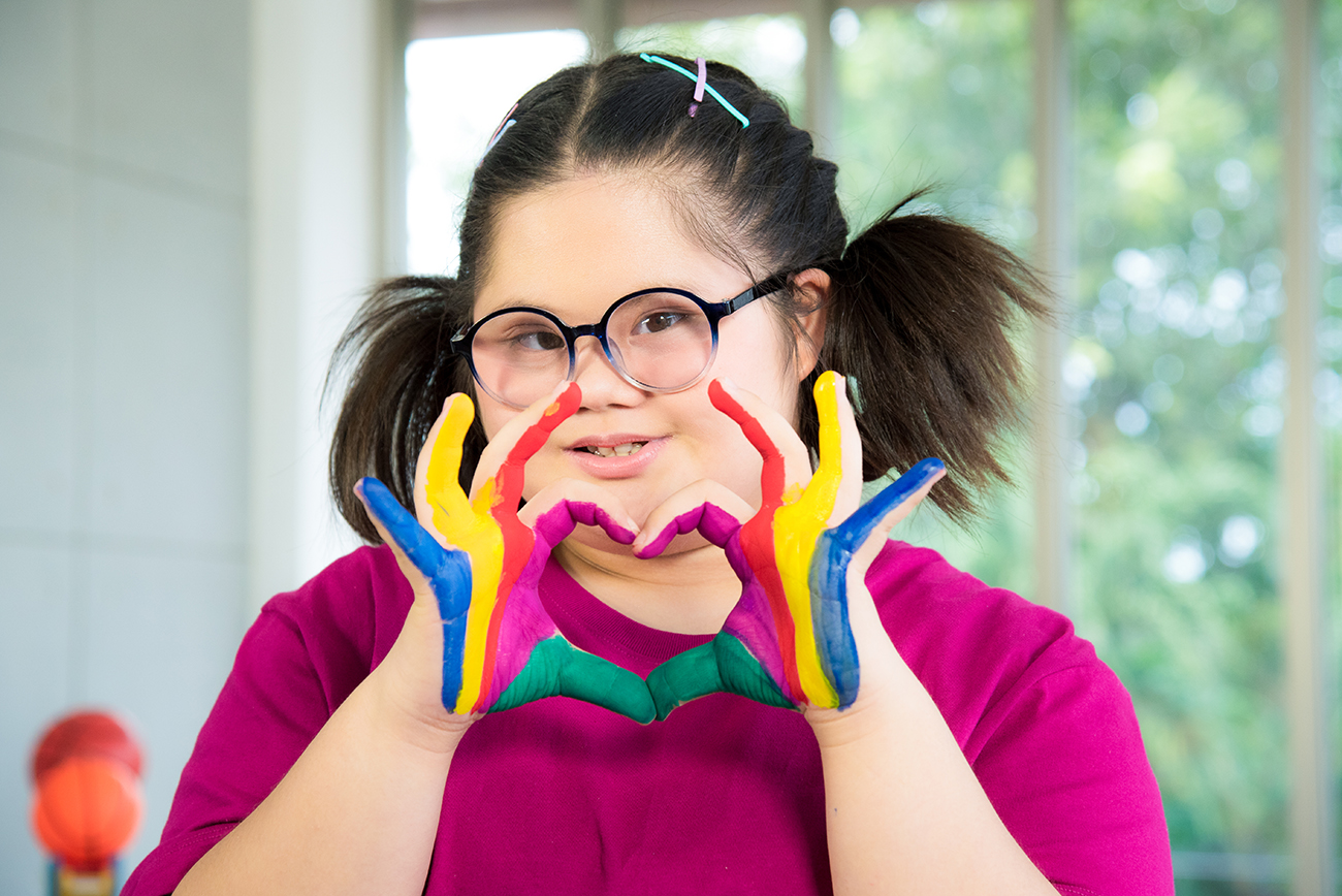 Retrato de una niña con síndrome de Down y manos pintadas de colores